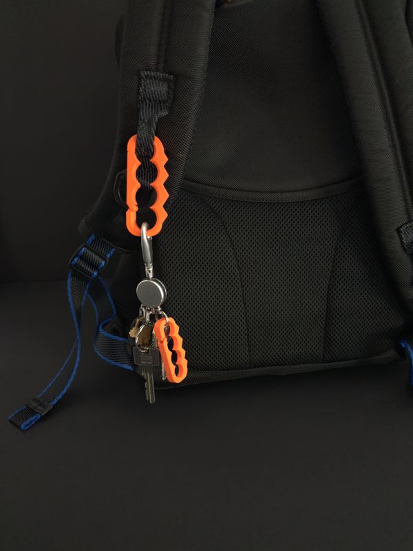 Orange TactiClutch clipped over a backpack strap, carrying a set of keys