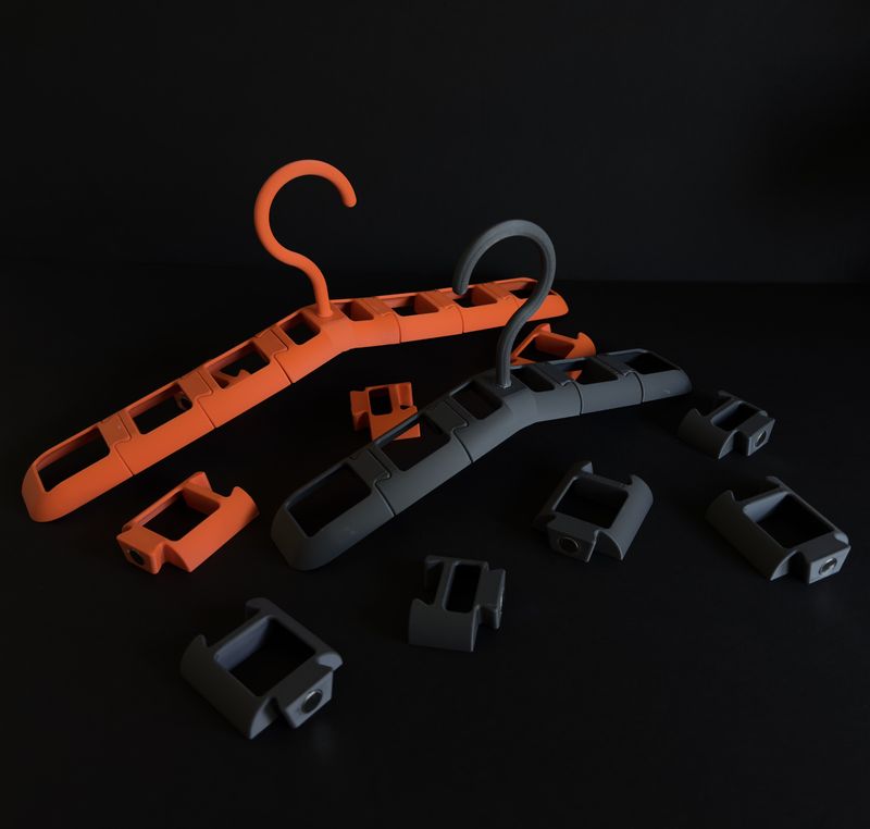 Two assembled TactiHang hangers in orange and grey on a dark background, surrounded by loose arm segments