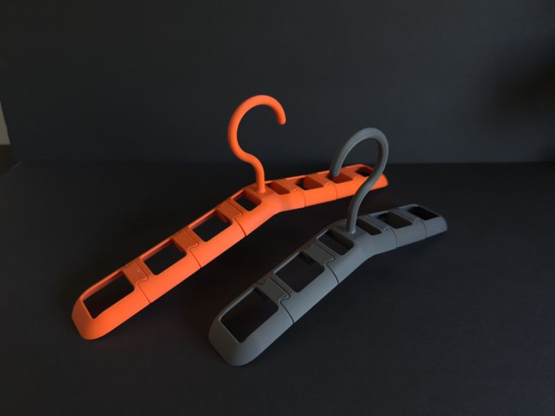 Two assembled TactiHang modular hangers, orange and grey, on a dark background